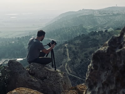 男人坐在岩石上使用相机
